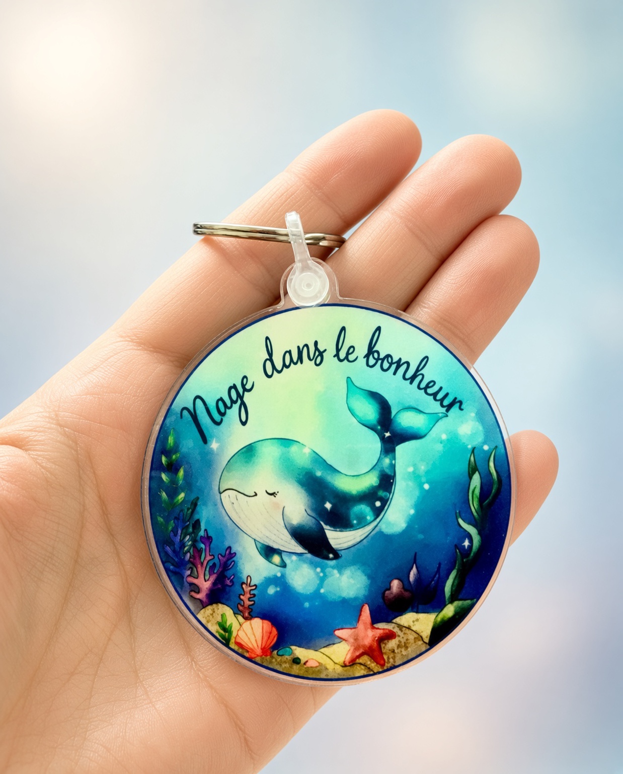 Porte-clés baleine Nage dans le bonheur en acrylique transparent, présenté dans une main
