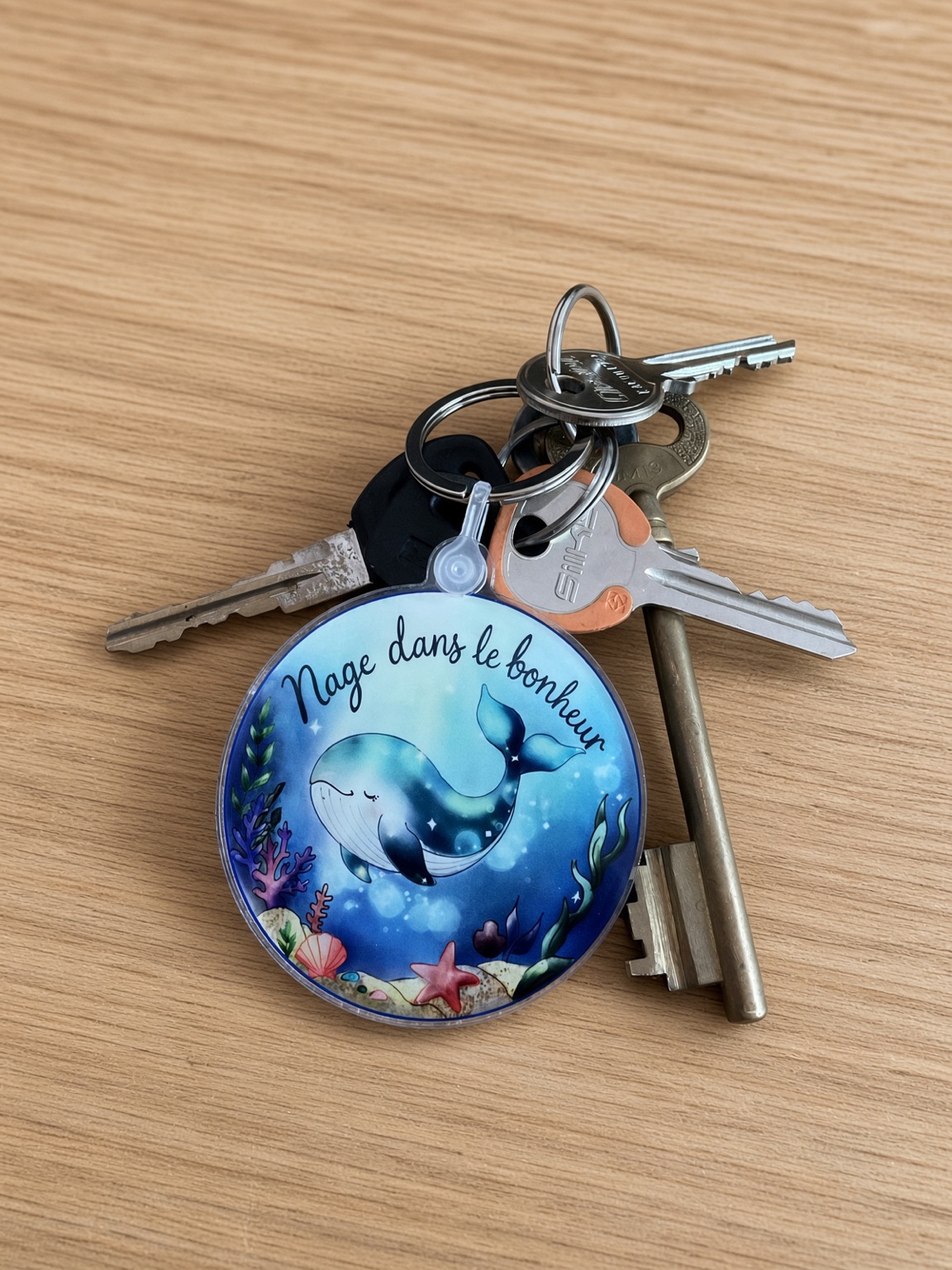 Porte-clés baleine Nage dans le bonheur attaché à un trousseau de clés sur une table
