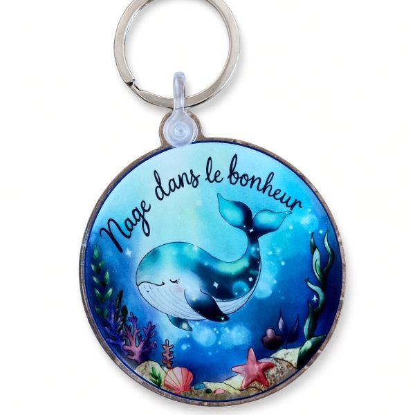Porte-clés rond en acrylique avec une baleine bleue et le message Nage dans le bonheur, sur fond blanc